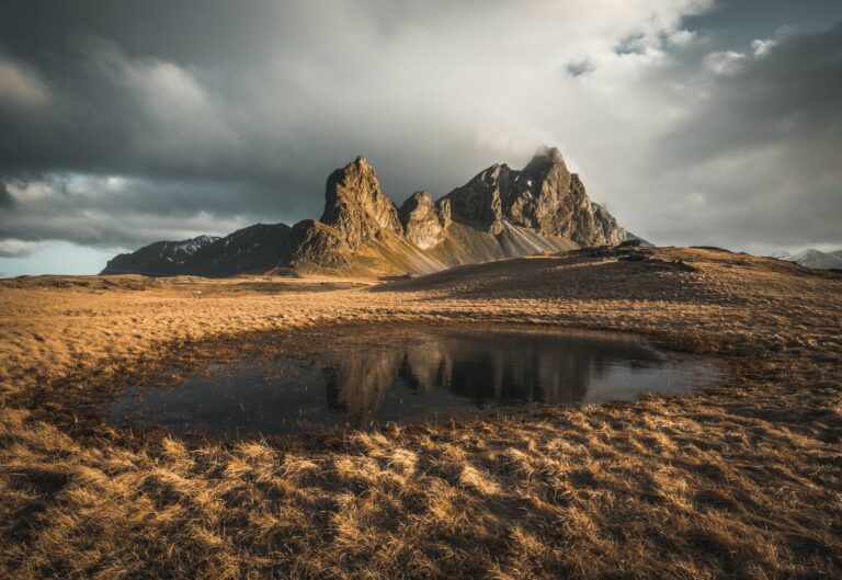 small puddle by steep rocks under grey sky